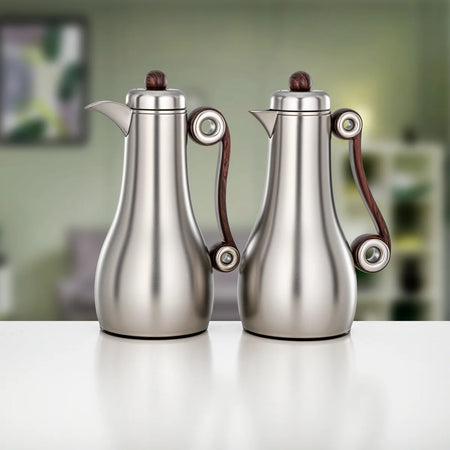 Two stainless steel coffee makers with dark brown wooden handles and matching dark brown lid knobs, displayed side-by-side on a white surface with a blurred green background.