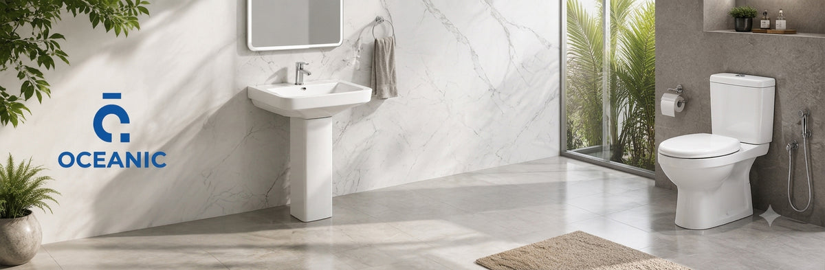 A modern bathroom scene featuring a white pedestal sink on the left and a white toilet on the right, set against marble-look walls and floor. A blue OCEANIC logo is visible on the left side.