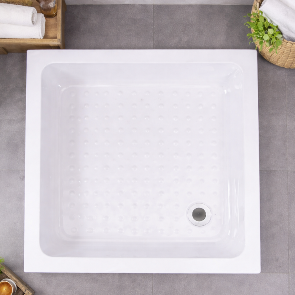 White rectangular shower tray on a gray tiled floor with towels and a plant.